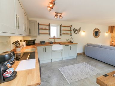 A kitchen area with wooden countertops and light green cabinets next to a living area with a grey sofa and a wall mirror at Robins Downs in Ilfracombe