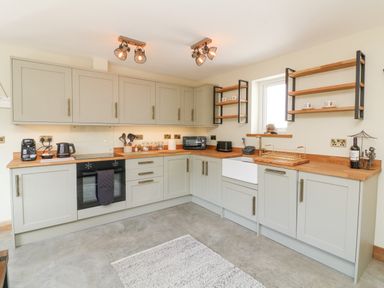 A kitchen with gray cabinets wooden countertops appliances and open shelves at Robins Downs in Ilfracombe