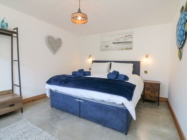 A bedroom with a bed with blue bedding bedside tables a heart shaped wall decoration and a large blue turtle decoration at Robins Downs in Ilfracombe