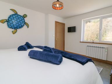 A bedroom with a bed with blue towels on it a wooden door a wall-mounted TV a window and a blue turtle decoration on the wall at Robins Downs in Ilfracombe