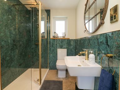 A bathroom with a shower enclosure toilet sink round mirror and window at Robins Downs in Ilfracombe