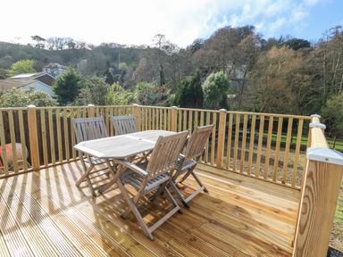 An outdoor wooden deck with a table and four chairs surrounded by a wooden railing at Robins Downs in Ilfracombe