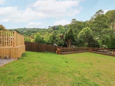 A grassy backyard with wooden fences and trees in the background at Robins Downs in Ilfracombe