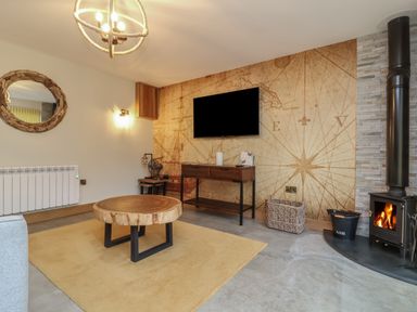 A living room with a round wooden coffee table a wall-mounted tv a wood-burning stove and a map wallpaper at Robins Downs in Ilfracombe
