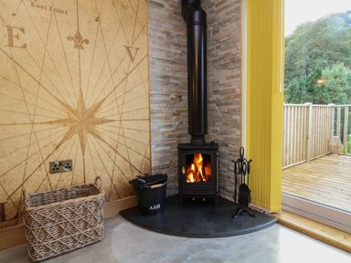 A corner with a wood burning stove next to a glass door leading to a wooden deck at Robins Downs Ilfracombe
