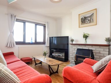 A living room with red covered sofas a wooden coffee table a television and a fireplace at Chi an Vre in Newlyn