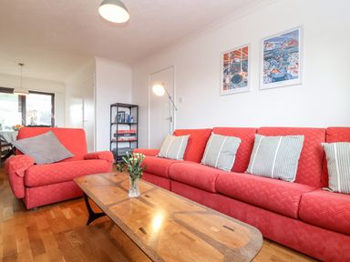 A living room with red sofas a wooden coffee table with flowers on it a black shelving unit and framed pictures on the wall at Chi an Vre in Newlyn