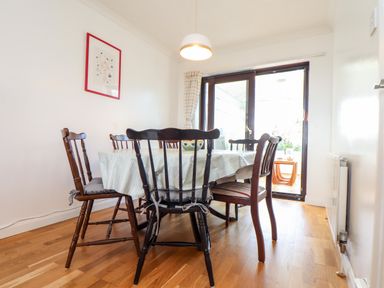 A dining room with a table covered by a tablecloth and six wooden chairs near glass doors at Chi an Vre in Newlyn