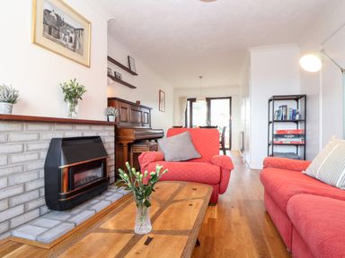 A living room with red sofas a wooden coffee table a fireplace a piano and shelves at Chi an Vre in Newlyn