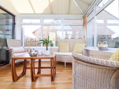 A conservatory with wicker chairs and loveseat a wooden table with teapot mugs and plants at Chi an Vre in Newlyn