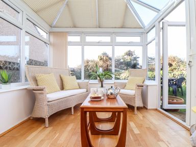 A conservatory with wicker sofa and armchair yellow cushions wooden coffee table with teapot and cake at Chi an Vre in Newlyn