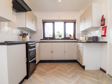 A kitchen with cabinets a stove a window with blinds and various kitchen utensils at Chi an Vre in Newlyn