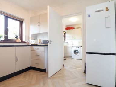 A kitchen with a white refrigerator beige cabinets utensils on the counter and a washing machine visible through an open door at Chi an Vre in Newlyn