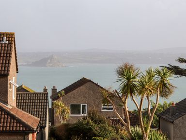 Houses with tiled roofs and palm trees overlooking the sea and a distant island at Chi an Vre in Newlyn