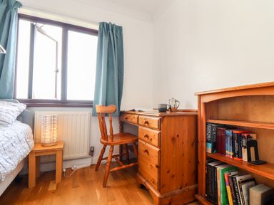A bedroom with a wooden desk and chair next to a window with blue curtains and a bookshelf with books at Chi an Vre in Newlyn