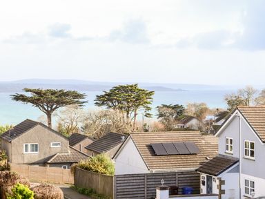 Houses with tiled roofs and solar panels near the coast with trees and sea in the background at Chi an Vre in Newlyn