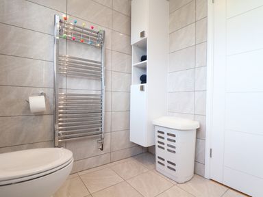 A bathroom with tiled walls and floor a white toilet a chrome towel radiator a wall cabinet and a laundry bin at Chi an Vre in Newlyn