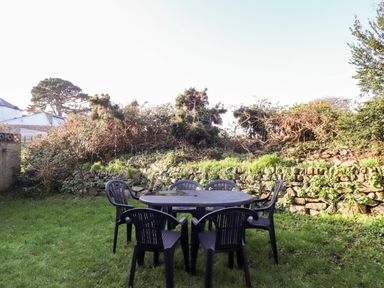 An outdoor garden area with a round black table and six black chairs on green grass at Chi an Vre in Newlyn