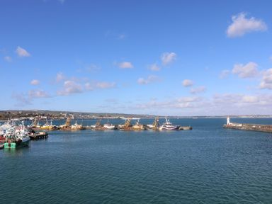 A harbor with fishing boats docked and a lighthouse on a pier at Chi an Vre in Newlyn