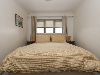 A bedroom with a bed covered in patterned bedding two bedside tables with lamps and a window with curtains and blinds at Chi an Vre in Newlyn