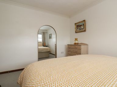 A bedroom with a bed a wooden chest of drawers a framed painting and an arched mirror on the wall at Chi an Vre in Newlyn