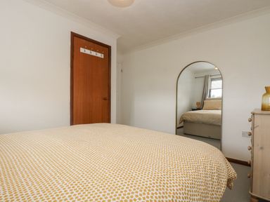 A bedroom with a bed covered with patterned bedding a wooden door a mirror and a chest of drawers at Chi an Vre in Newlyn
