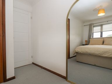 A bedroom with a bed a bedside table with a lamp window with blinds and curtains and a mirror with a wooden frame at Chi an Vre in Newlyn