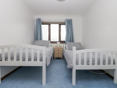A bedroom with two single beds striped bedding blue carpet and wooden nightstand at Chi an Vre in Newlyn