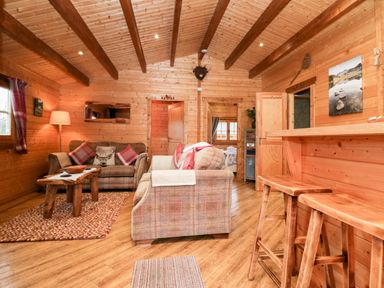 A wooden living room with two sofas a wooden coffee table and a bar area with stools at Ballinorig Lodge in Cleator Moor