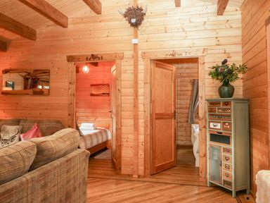 A wooden interior room with a sofa on the left two doorways in the center and a tall cabinet with a vase of flowers on the right at Ballinorig Lodge in Cleator Moor
