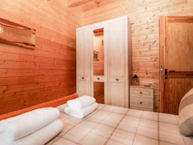 A bedroom with wooden walls a bed with folded towels a wardrobe and a chest of drawers at Ballinorig Lodge in Cleator Moor