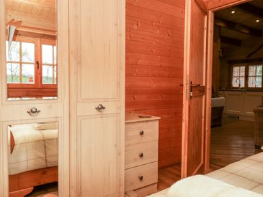 A bedroom with wooden wardrobe with mirror and a small chest of drawers next to an open door leading to a kitchen at Ballinorig Lodge in Cleator Moor