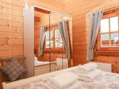 A wooden bedroom with a bed that has folded towels a mirror wardrobe and a chair with a cushion at Ballinorig Lodge in Cleator Moor