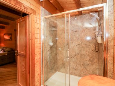 A wooden bathroom with a glass shower enclosure and marble walls at Ballinorig Lodge in Cleator Moor