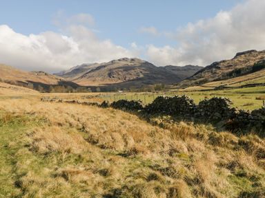 A rural landscape with grassy fields stone walls and hills under a partly cloudy sky at Ballinorig Lodge in Cleator Moor