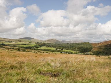 A grassy field with hills and trees under a cloudy sky at Ballinorig Lodge in Cleator Moor