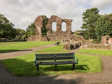 A park with a stone ruin and benches on grass surrounded by trees at Ballinorig Lodge in Cleator Moor