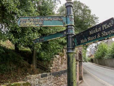A street signpost with directional signs near a stone wall and trees at Ballinorig Lodge in Cleator Moor