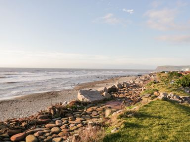 A rocky beach with waves hitting the shore grassy area with rocks and benches by the sea at Ballinorig Lodge in Cleator Moor