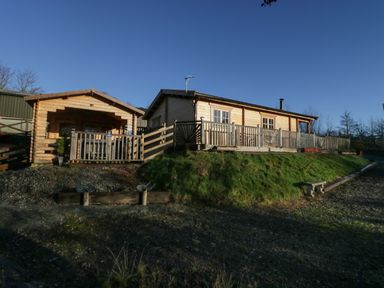 A wooden cabin with a fenced porch and wooden bench outside at Ballinorig Lodge in Cleator Moor