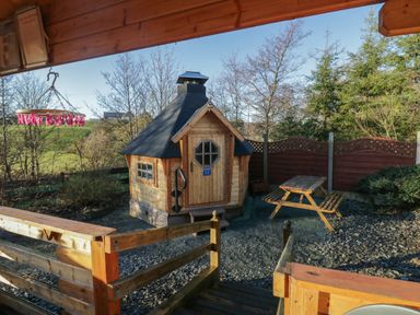 An outdoor wooden sauna cabin with a picnic table and wooden fence in a garden area at Ballinorig Lodge in Cleator Moor