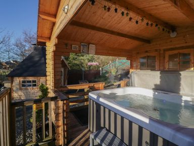 An outdoor covered wooden patio with a hot tub and wooden railings at Ballinorig Lodge in Cleator Moor