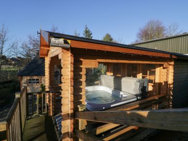 An outdoor wooden cabin with a covered hot tub on a wooden deck at Ballinorig Lodge in Cleator Moor