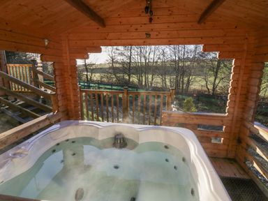 A wooden outdoor gazebo with a hot tub overlooking a fenced garden at Ballinorig Lodge in Cleator Moor