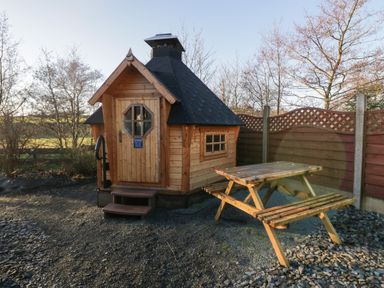 A small wooden cabin with a black roof next to a wooden picnic table in an outdoor area at Ballinorig Lodge in Cleator Moor