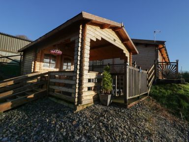 An exterior view of a wooden log cabin with a porch and ramp surrounded by rocks and grass at Ballinorig Lodge in Cleator Moor