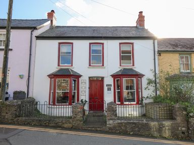 Exterior of a two story house with red door and window frames and a small front garden at Ty Len in St Davids
