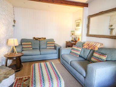 A living room with two blue sofas patterned cushions an ottoman wooden side table with a lamp and a large mirror on the wall at Ty Len in St Davids