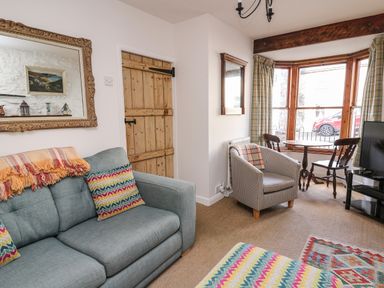 A sitting room with a blue sofa, armchair, wooden table with two chairs by a bay window, and a television at Ty Len in St Davids