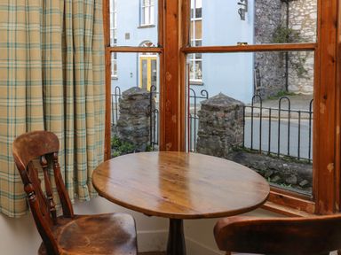A wooden round table with two wooden chairs by a window with plaid curtains at Ty Len in St Davids